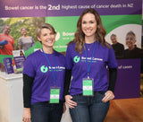 Two women in Bowel Cancer New Zealand branded tee-shirts with brochures and posters behind them