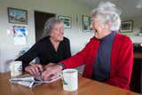 An elderly woman and visitor share a cup of tea