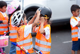 Children in high visibility vests putting on cycle helmets