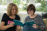 Two women sit together looking through a breast cancer handbook